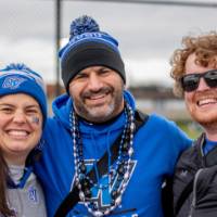 Three alumni smile and give the "anchor up" sign